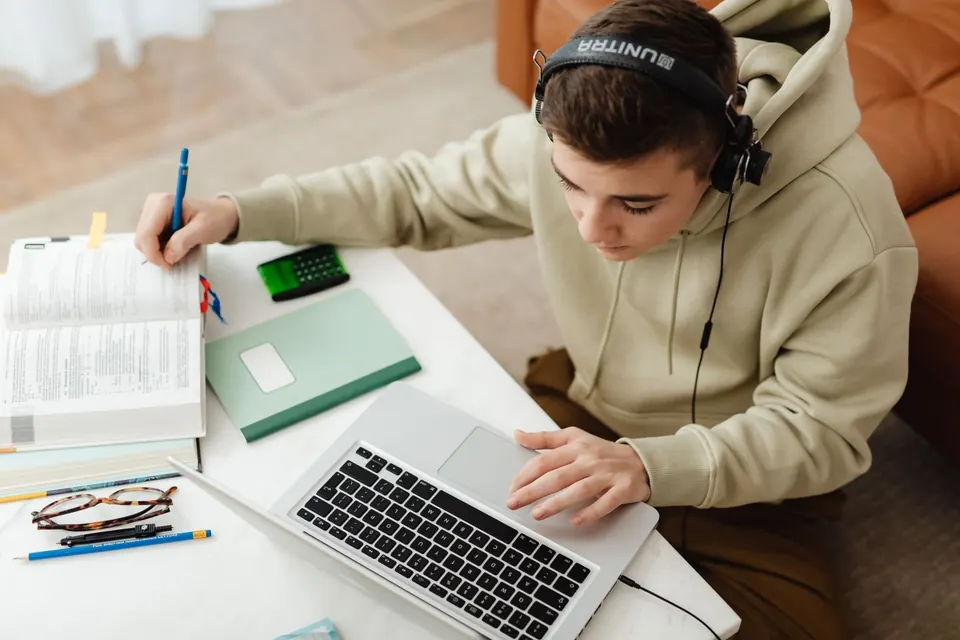Estudiante con auriculares frente a una notebook, con libros sobre el escritorio