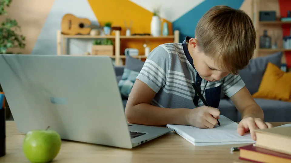 Niño estudiando con una notebook y escribiendo en un cuaderno
